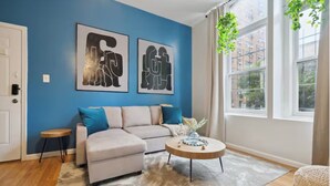 A living room with a blue wall, a beige sofa, a round coffee table, and a small side table. - Modern  Bright 1-bedroom condo in Rittenhouse Square- Center City Philadelphia (Philadelphia)