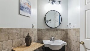 A bathroom with a round mirror, a sink, and a wooden table with a decorative item. - Modern  Bright 1-bedroom condo in Rittenhouse Square- Center City Philadelphia (Philadelphia)