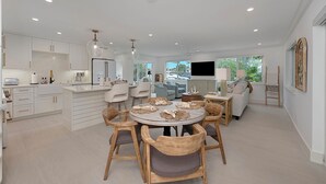 Cozinha moderna com armários brancos, área de refeições com cadeiras de madeira e uma janela grande que proporciona iluminação natural.