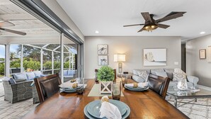 Un coin repas avec une table en bois, des chaises et un ventilateur de plafond. On y trouve également une table basse en verre, une lampe et une plante.