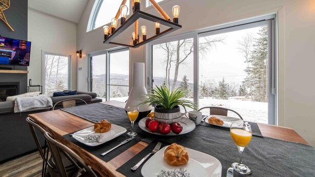 A dining area with a table set for breakfast, including croissants, fruit, and orange juice. - Petite Ourse 61: Hot Tub, Views &  Private Trails (Les Éboulements)