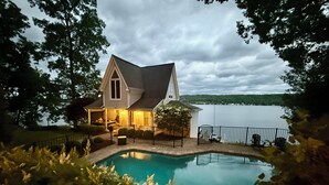 Une maison avec une piscine, entourée d’arbres et bordée d’un lac.