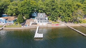 Une propriété au bord du lac, dotée d’un quai, d’une grande maison avec un toit à pignon bien visible et d’une forêt dense en arrière-plan.