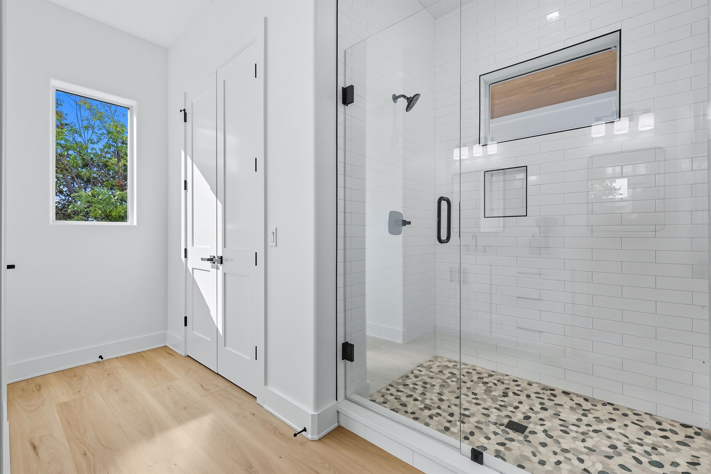 A modern bathroom with a glass-enclosed shower, white tiled walls, and a wooden floor.