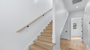 En moderne trappe med trætrin og gelænder, der fører hen til en dør med udsigt over grønne omgivelser.