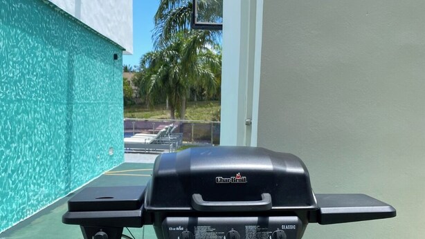 Un barbecue au gaz portatif, doté de commandes et d’un brûleur latéral, placé sur une surface verte à l’extérieur.