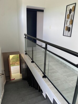 Uma escadaria moderna com guarda-corpos de vidro e vista para o exterior.