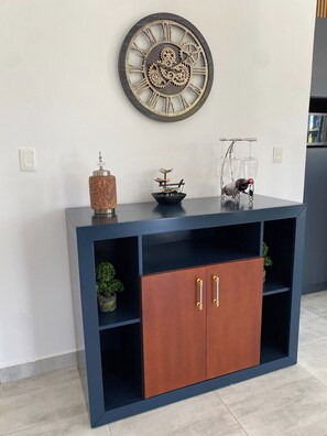 Uma sala de estar moderna com um armário azul escuro, um relógio decorativo e um pequeno modelo de navio em cima.