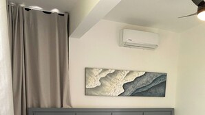 Une chambre à coucher avec un lit, une tête de lit, un climatiseur fixé au mur, un tableau et un rideau.