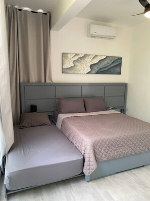 A bedroom with a bed, a headboard, a wall-mounted air conditioner, a painting, and a curtain. - Villa Tula.  An oasis of tranquility for the whole family in Sosua. (Sosúa)