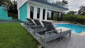 Une maison moderne à deux étages, dotée d’une piscine, d’un espace de détente extérieur et d’un terrain de basketball.