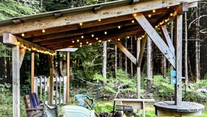 Une pergola en bois rustique, agrémentée de guirlandes lumineuses, avec des sièges d’extérieur et une table rustique.