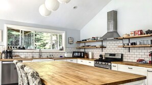 Une cuisine moderne dotée d’un grand îlot central, de carreaux de métro blancs, d’appareils électroménagers en acier inoxydable et de plans de travail en bois.