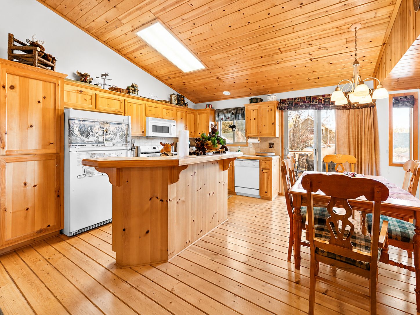 Interior de una cabaña de madera con cocina, comedor y un amplio ventanal.