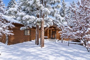 A wooden cabin with a porch, surrounded by snow-covered trees.