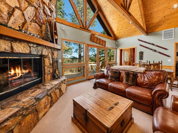 A spacious living room with a stone fireplace, leather furniture, and large windows offering a view of the outdoors.