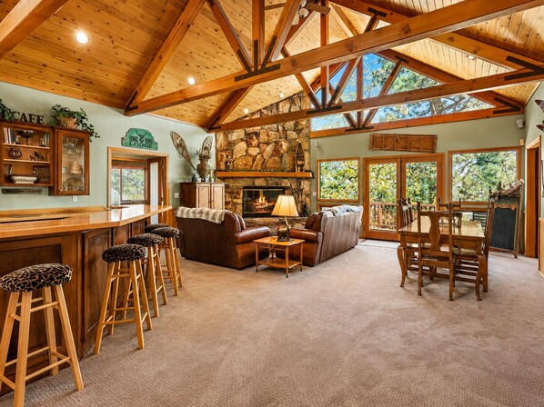 A spacious living area with a stone fireplace, wooden ceiling beams, and a bar with stools.