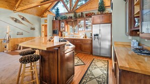 A spacious kitchen with wooden beams, a large island with stools, and a refrigerator. - The Getaway Chalet - Walk to Slopes & Golf Course, Ping Pong, Fireplace, Deck (Big Bear Lake)