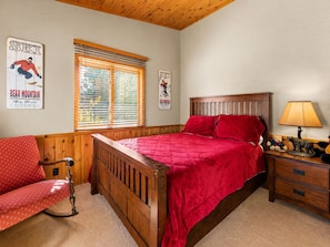 Un dormitorio con una cama de madera, una silla roja, una mesita de noche con una lámpara y dos carteles en la pared.