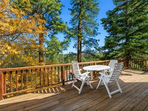 A wooden deck with a table and chairs, surrounded by trees with autumn foliage.