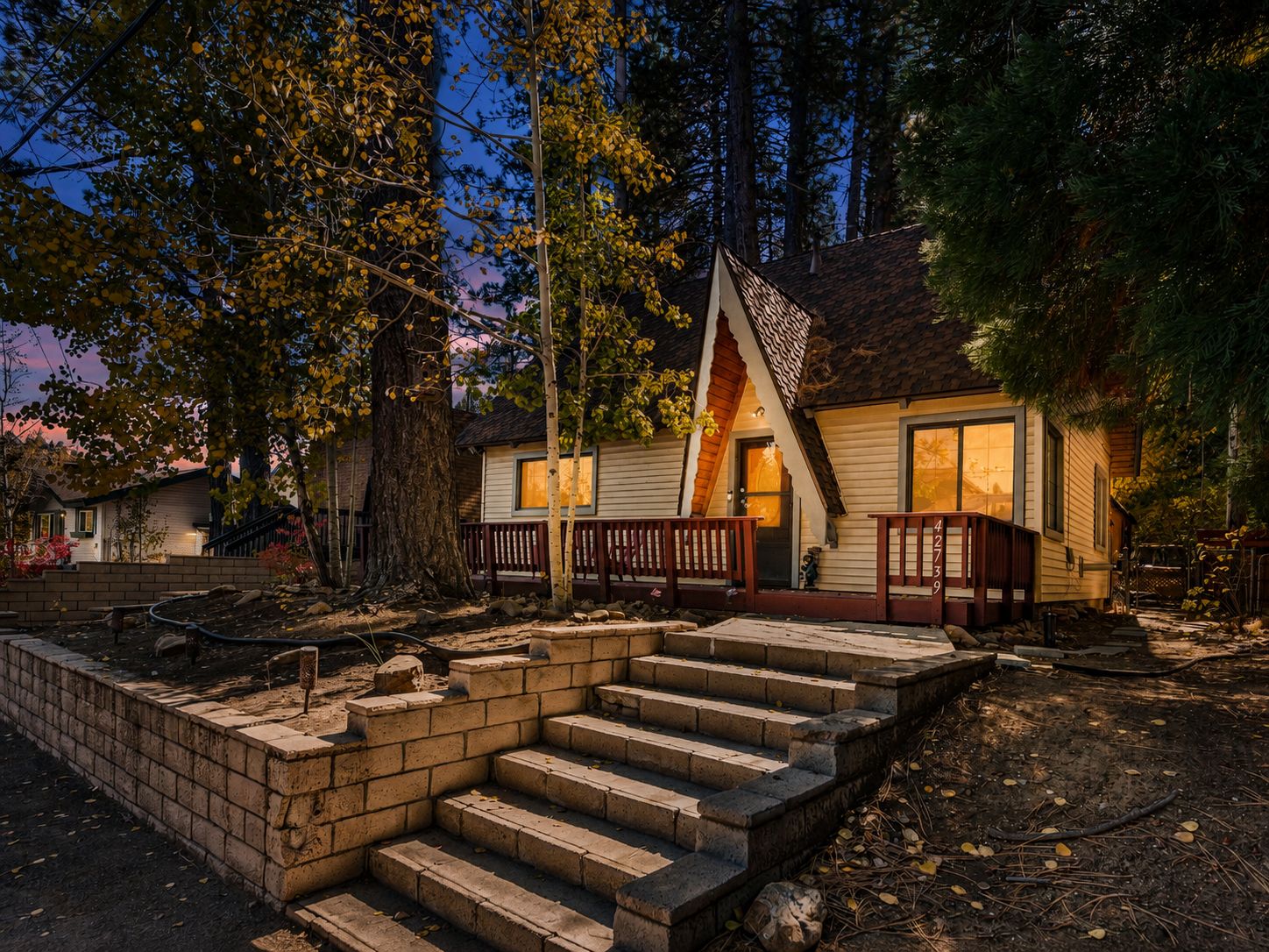 A cabin with a wooden deck, a set of stone steps leading to the entrance, and a large tree in the foreground.