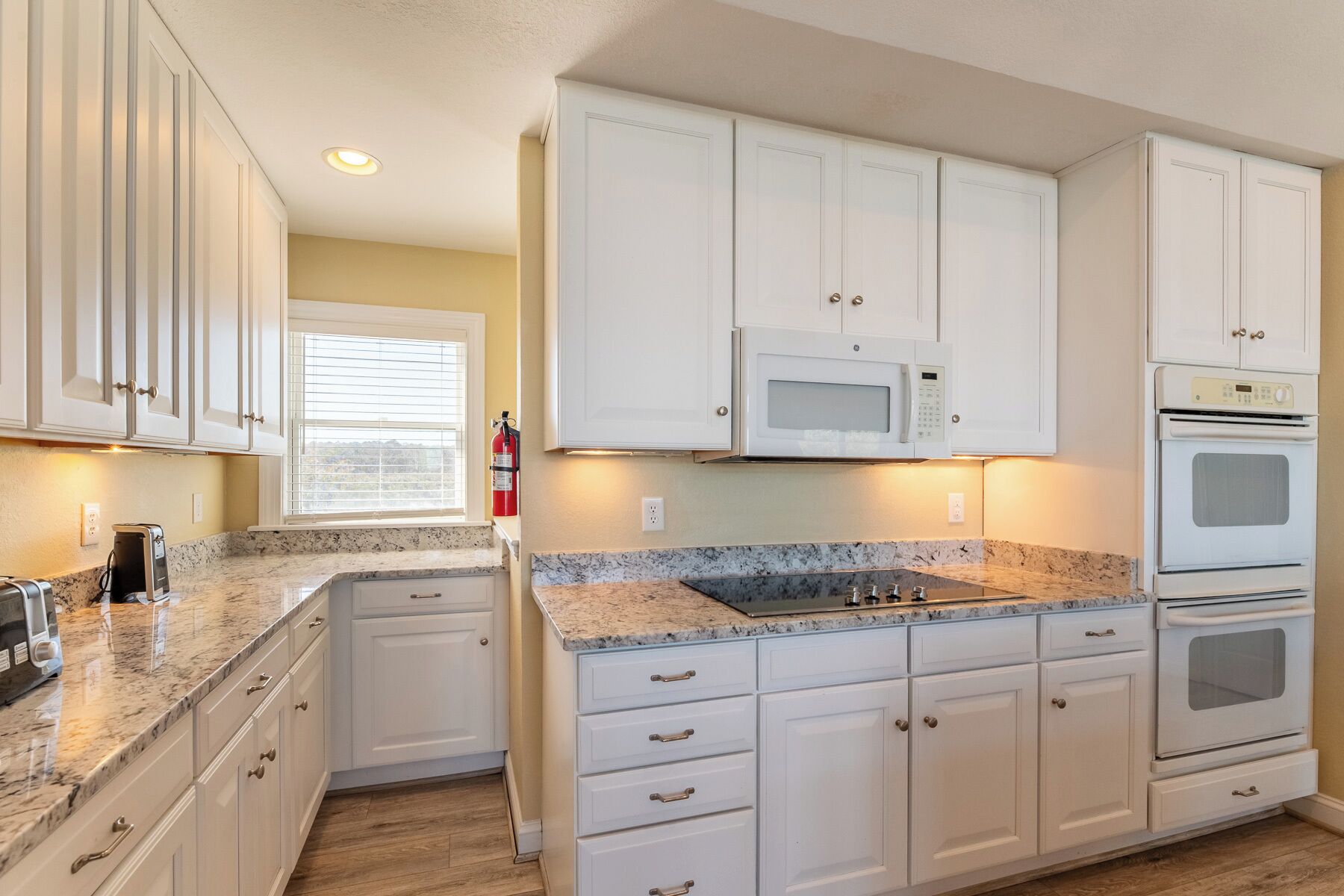 A kitchen with white cabinets, a microwave, an oven, and a coffee maker.