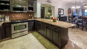 Cozinha moderna com bancadas de granito, eletrodomésticos de aço inoxidável e armários escuros.
