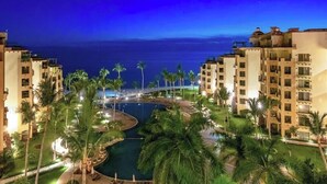 Resort com piscina cercada por palmeiras e edifícios à beira-mar.