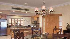 Cozinha moderna com ilha central, armários de madeira e área de refeições com mesa e cadeiras de vidro.