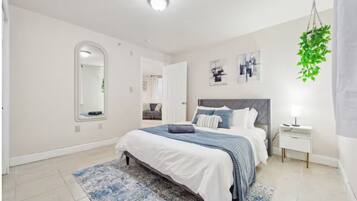 A modern bedroom with a large bed, a bedside table, a hanging plant, and a mirror.