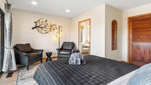 Ein Schlafzimmer mit einem großen Bett, zwei Stühlen, einem Spiegel und einer Holztür.