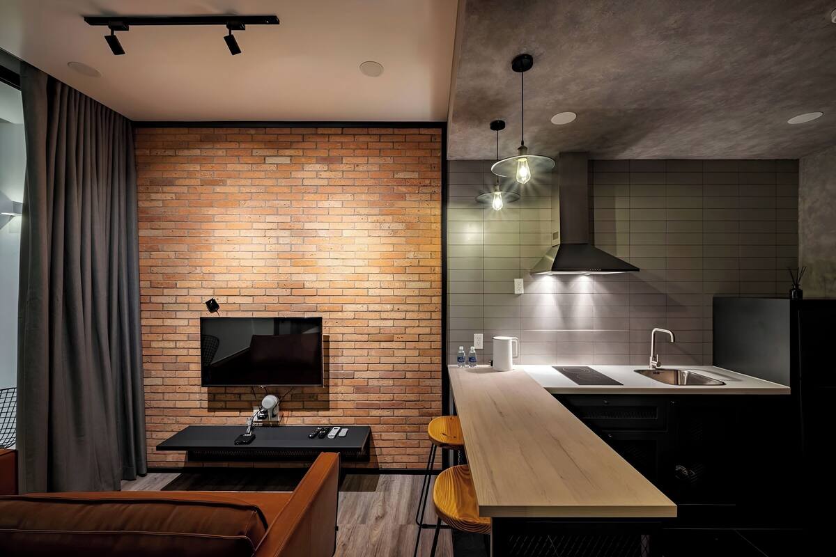 A modern kitchen with a brick wall, a wooden dining table, and a built-in TV.