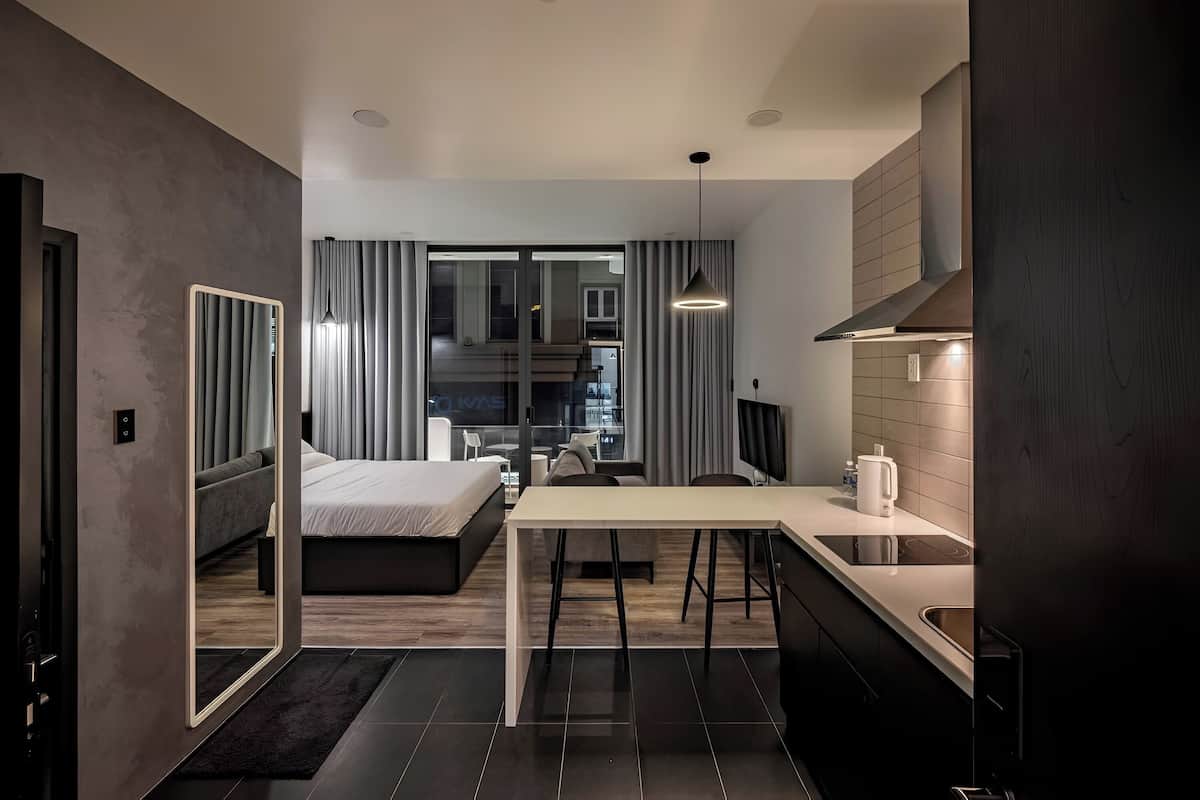 A modern hotel room with a bed, a dining area, and a kitchen.