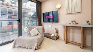 Un soggiorno moderno con una grande TV che mostra “NETFLIX”, un divano, un tavolino consolle in legno e vista attraverso una porta scorrevole in vetro.