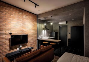 Ein modernes Hotelzimmer mit einer Ziegelfassade, einem Flachbildfernseher, einem Ledersofa, einer kleinen Küchenzeile mit Spüle und Barhocker sowie einem großen Bett.
