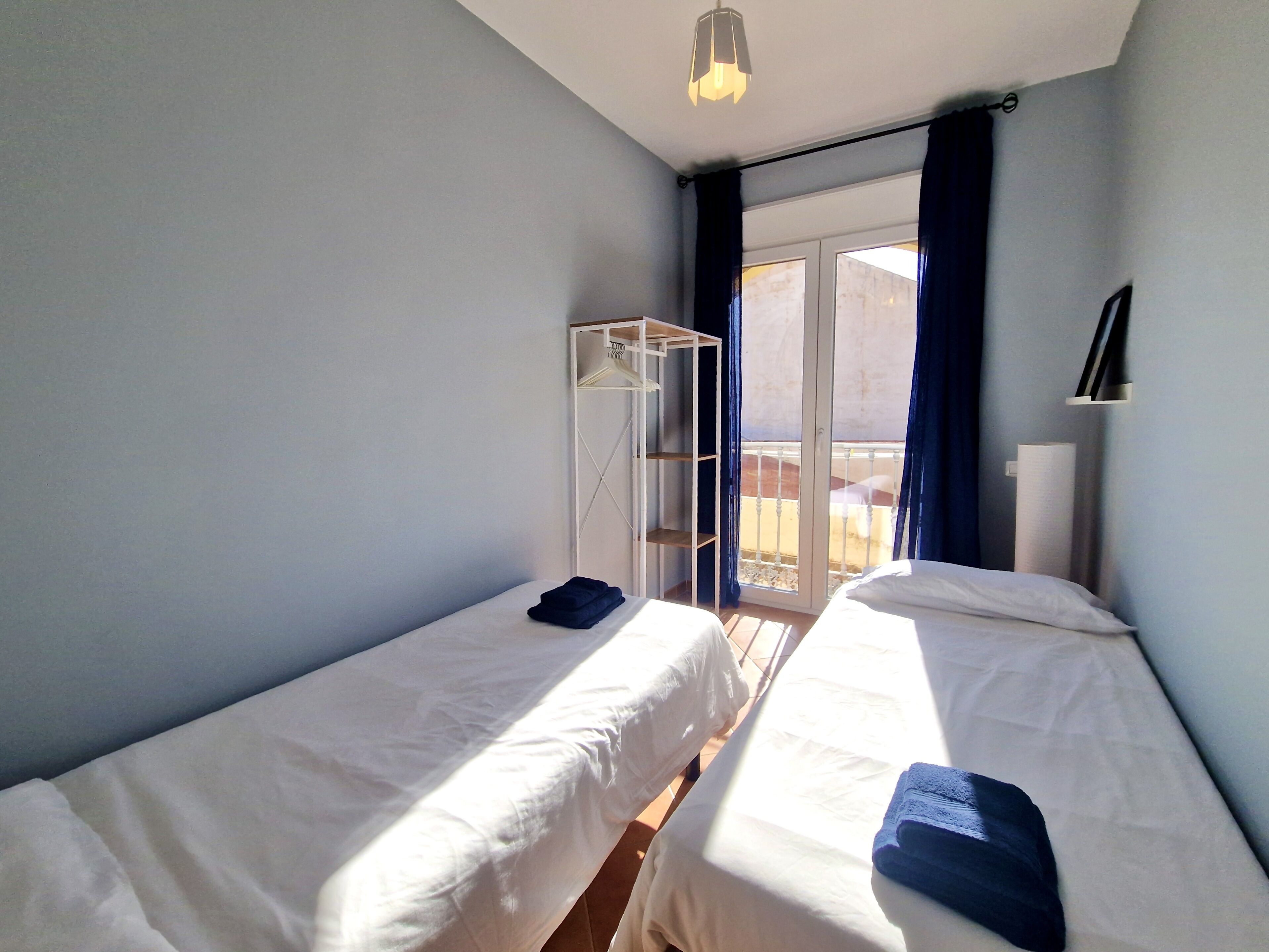 Ein Zimmer mit zwei Einzelbetten, einem Schrank, einem Balkon mit Geländer und einer Deckenleuchte.