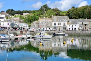 A harbor with boats docked, buildings with shops, and a hillside in the background.