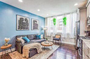 Una sala de estar moderna con una pared azul de acento, un sofá gris, una mesa de centro redonda y una zona de cocina con estufa.