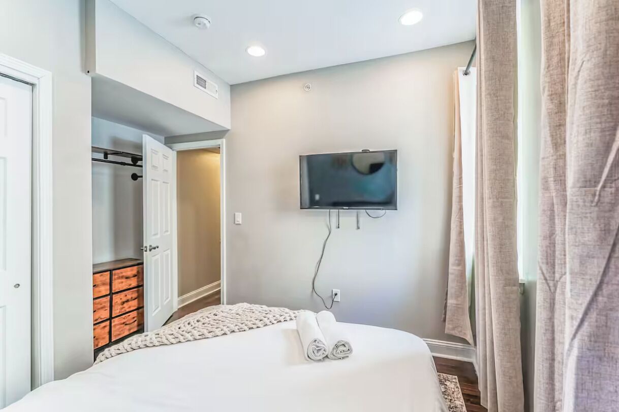 A hotel room with a bed, a TV mounted on the wall, a wardrobe, and a door leading to a bathroom.