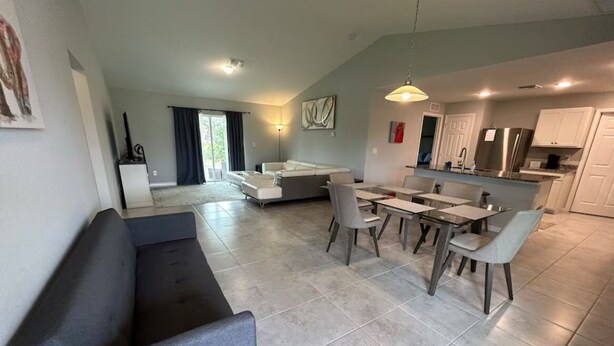 A modern living room with a grey sofa, dining area with a table and chairs, and a kitchen with white cabinets and a stainless steel refrigerator. - 3-bedroom house in welcoming Port Charlotte with AC (Port Charlotte)