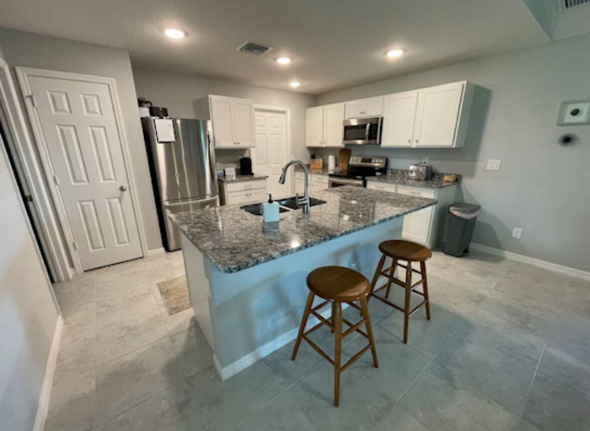 A kitchen with a granite countertop, stainless steel appliances, and wooden stools. - 3-bedroom house in welcoming Port Charlotte with AC (Port Charlotte)