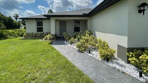A modern two-story house with a paved driveway, a well-maintained lawn, and small shrubs along the pathway. - 3-bedroom house in welcoming Port Charlotte with AC (Port Charlotte)