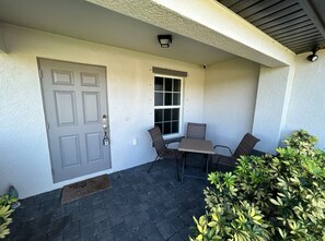 Une terrasse couverte avec une porte, une fenêtre et une table entourée de chaises.
