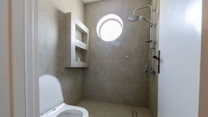 A small, modern bathroom with a toilet, a shower, and a round mirror. - Han Dhahrat Laban (Riyadh)
