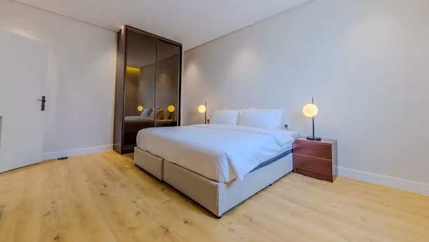 A modern bedroom with a large bed, a wooden floor, a wardrobe with a mirror, and bedside lamps. - Han Dhahrat Laban (Riyadh)