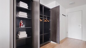 Ein begehbarer Kleiderschrank mit geöffneten Türen, Regalen mit gefalteten Handtüchern und einer Kleiderstange, sowie ein rostiersoniges Eisen.