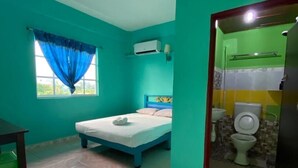 A room with teal walls, a bed, a window with blue curtains, a small table, and a bathroom with a toilet and sink. - Zackry Guesthouse (Langkawi)