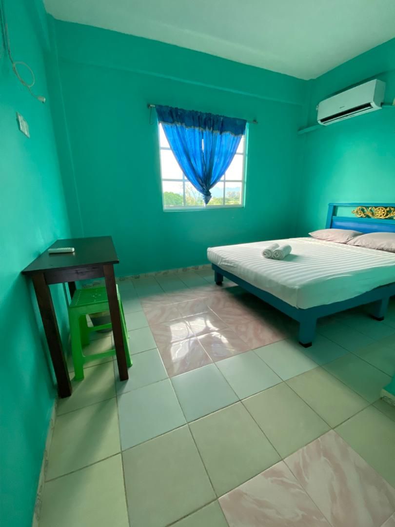 A room with teal walls, a bed with a blue headboard, a window with blue curtains, and an air conditioning unit on the wall.