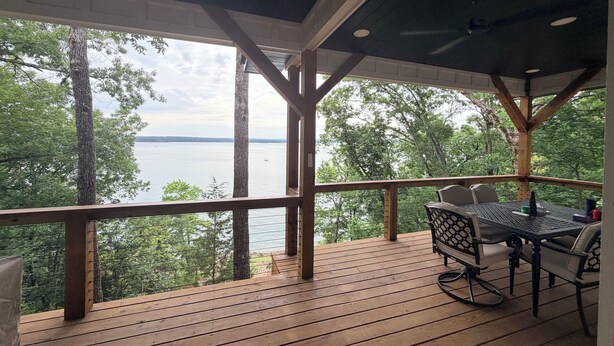 A wooden deck with a table and chairs, overlooking a body of water and trees.