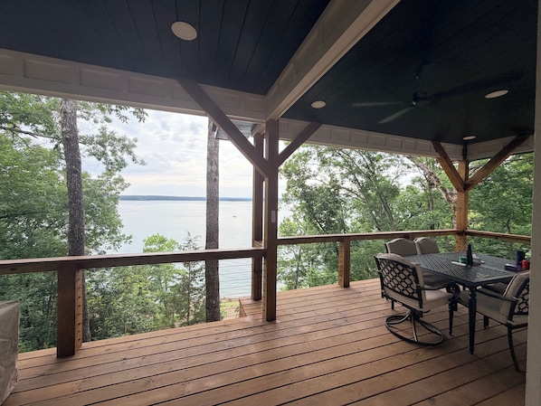 A wooden deck with a table and chairs, overlooking a body of water and trees.